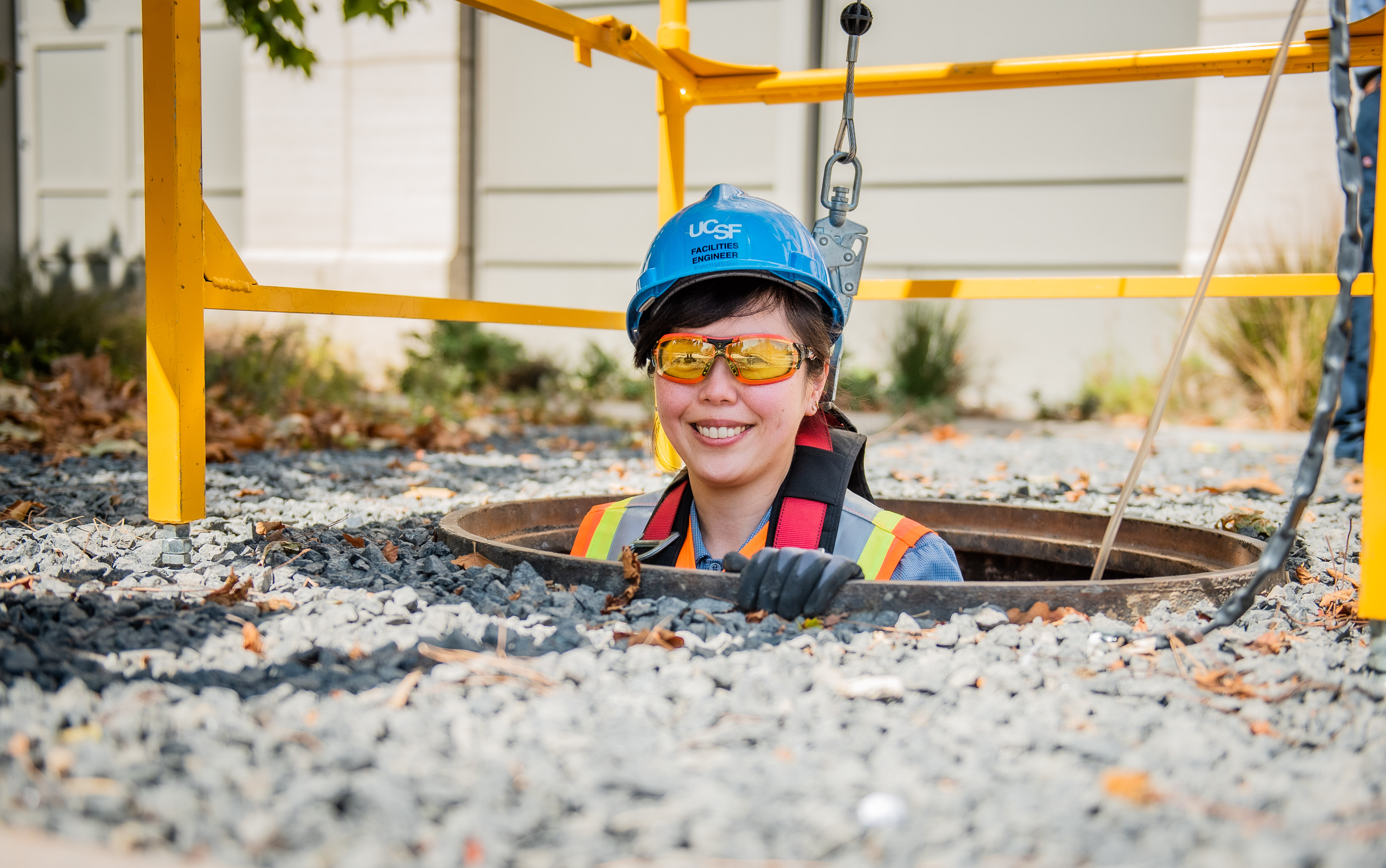A woman with a hard hat emerging from a mahole.