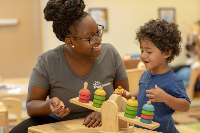 Preschool teacher using wooden toy to teach child about weights.