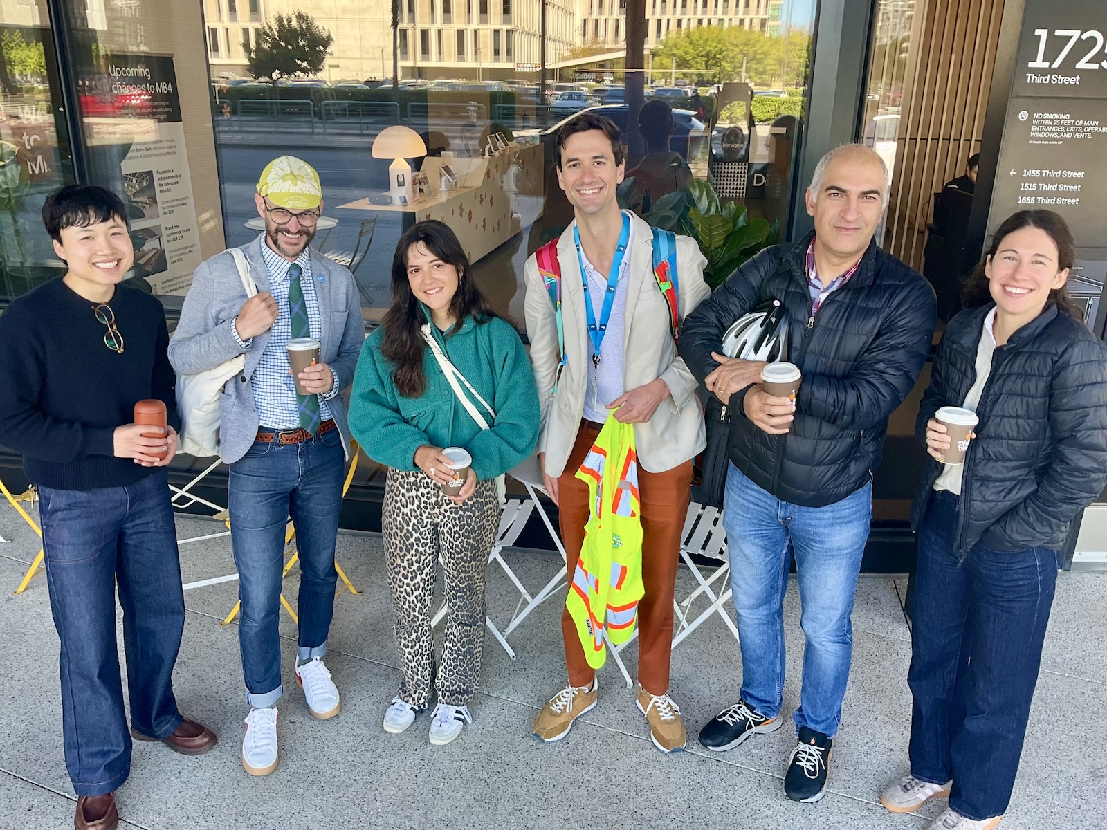 A group of diverse people stand holding coffee cups and smiling
