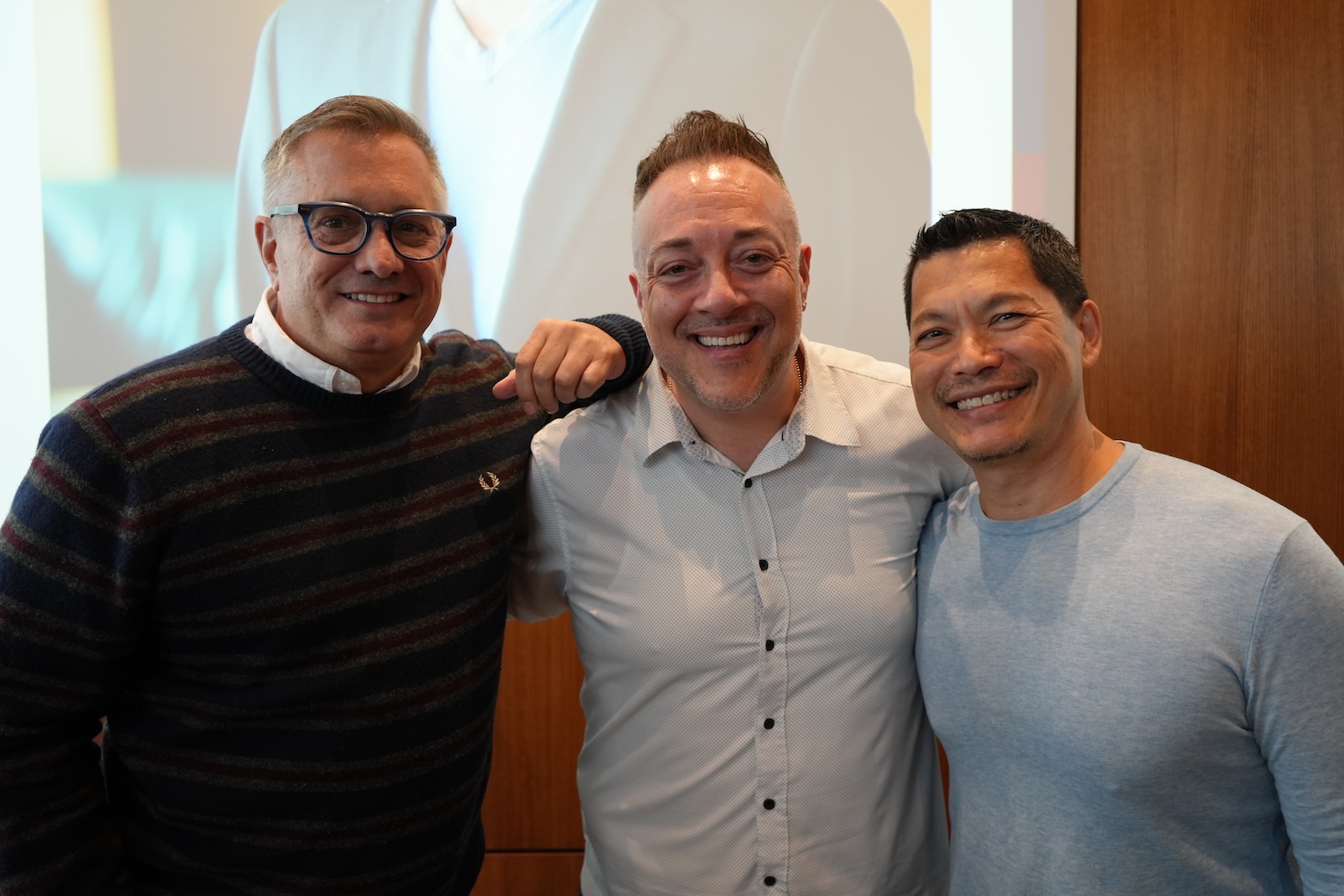 Three men pose in front of a presentation