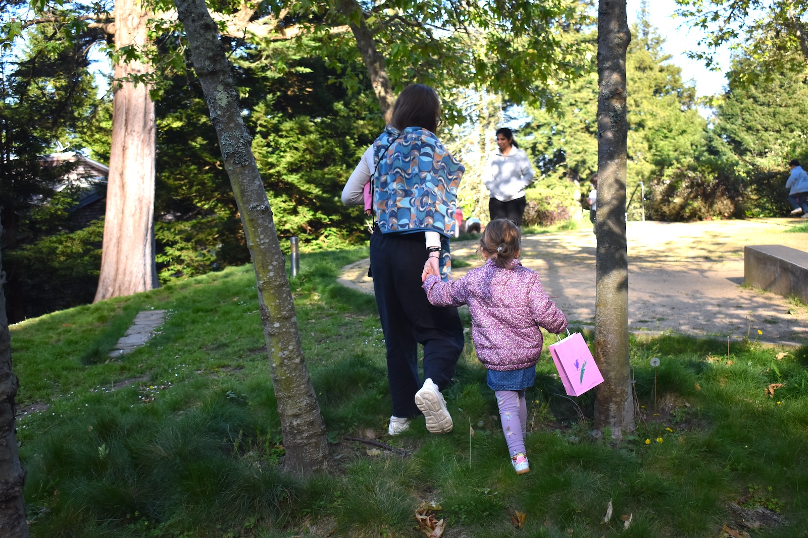 A woman and child walk hand in hand across the grass