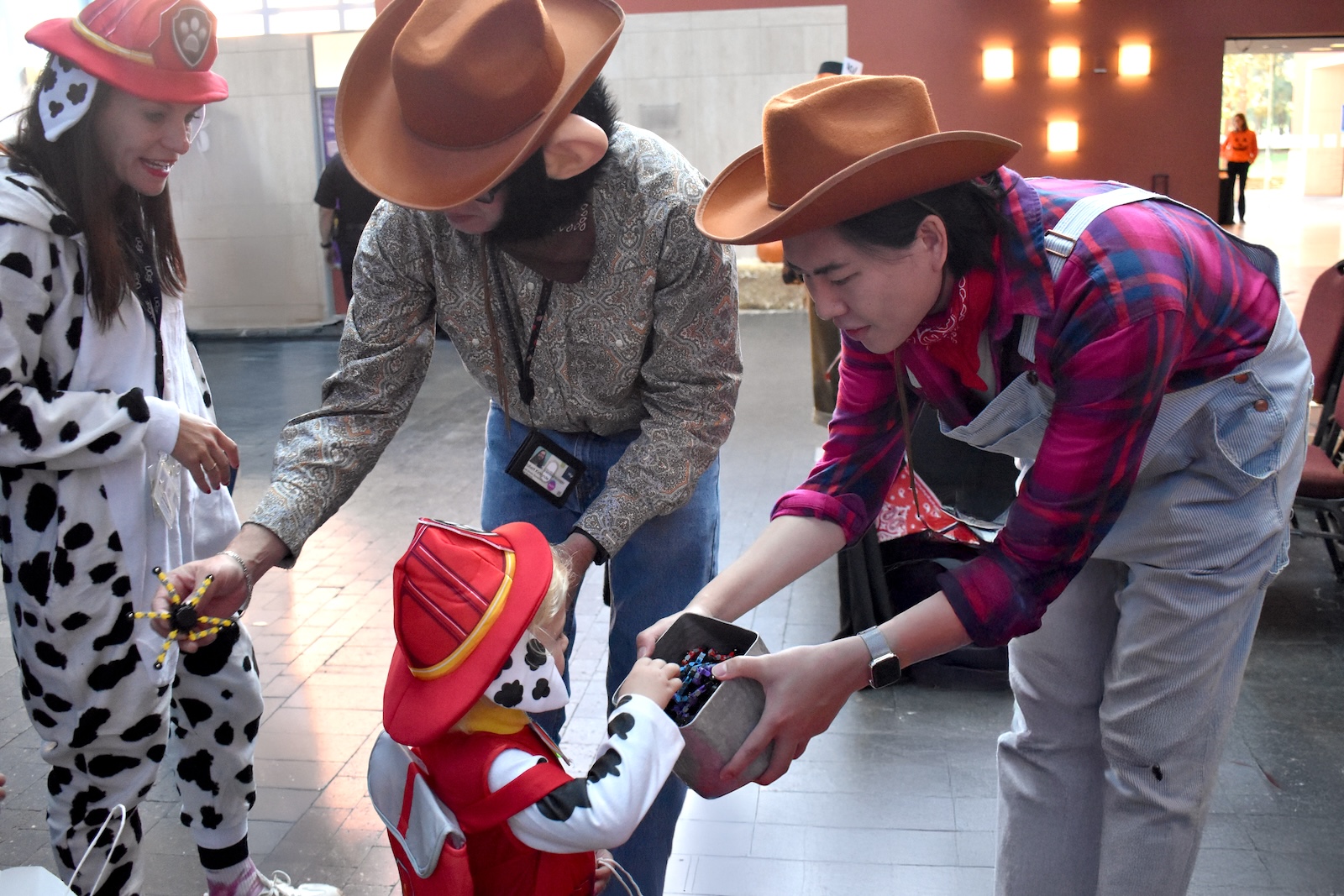 Child dressed as a firefighter trick-or-treats at Arts and Events table. 