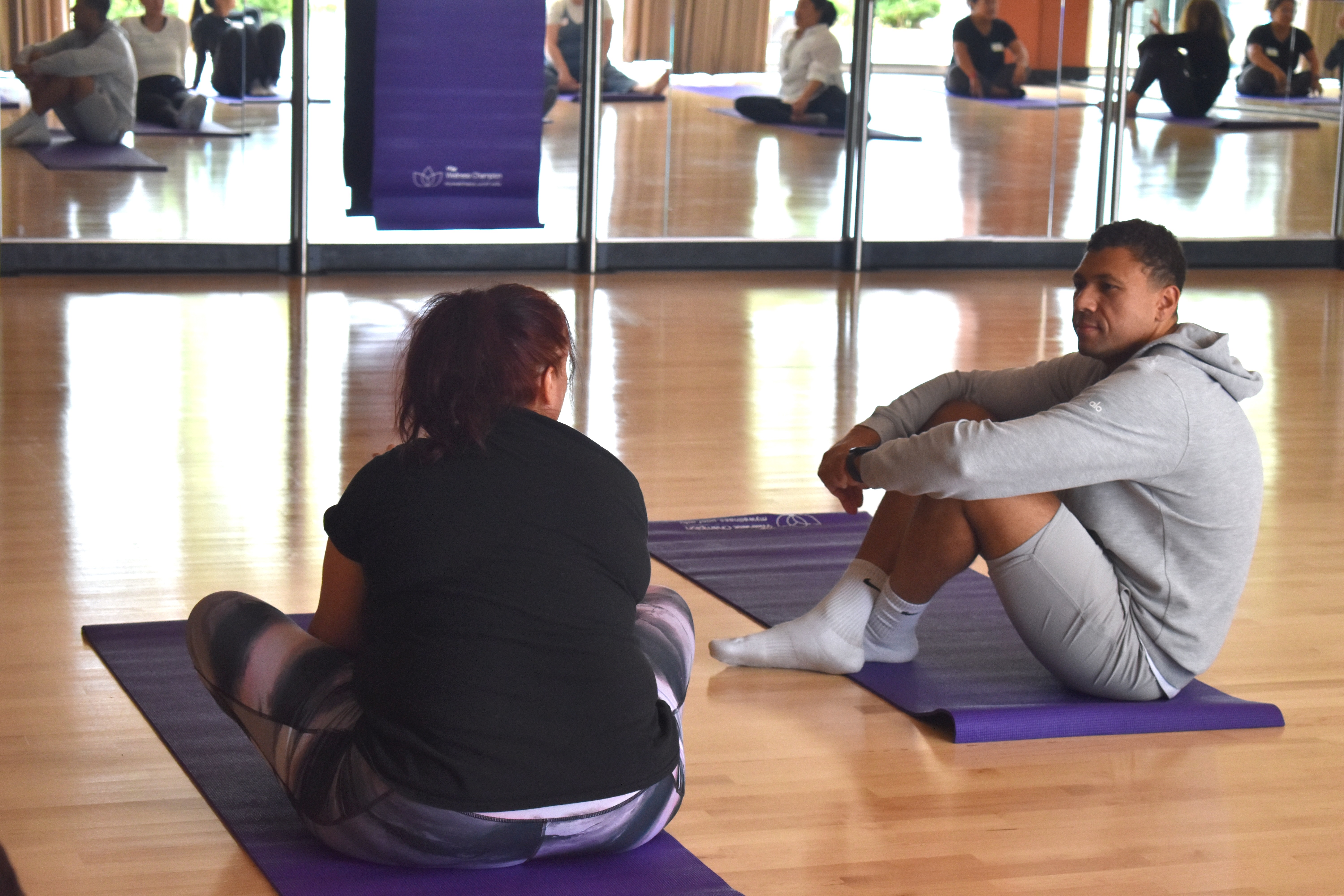A man and woman speak together while sitting on yoga mats