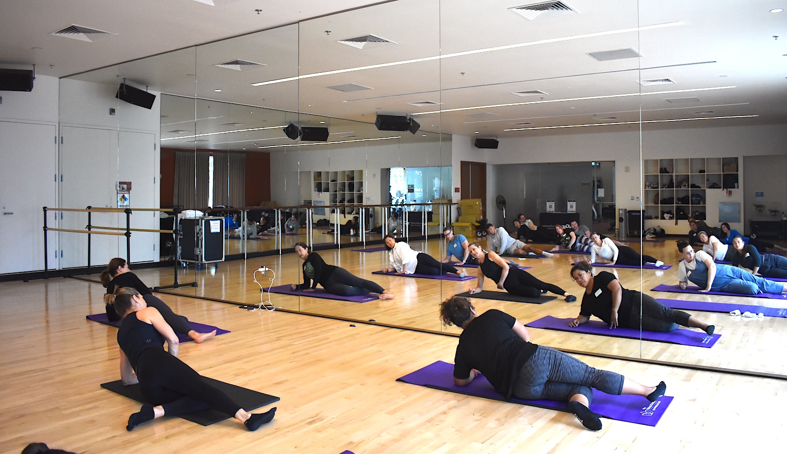 Yoga students balance with their sides on mat while looking at themselves in the mirror.