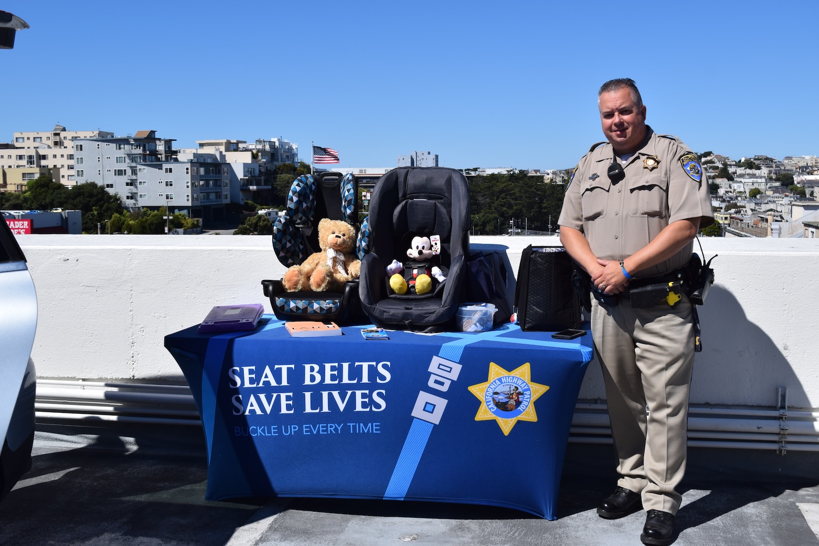 CHP Officer Mark Andrews stands in front of demonstration table, table cloth reads Seatbelts Save Lives