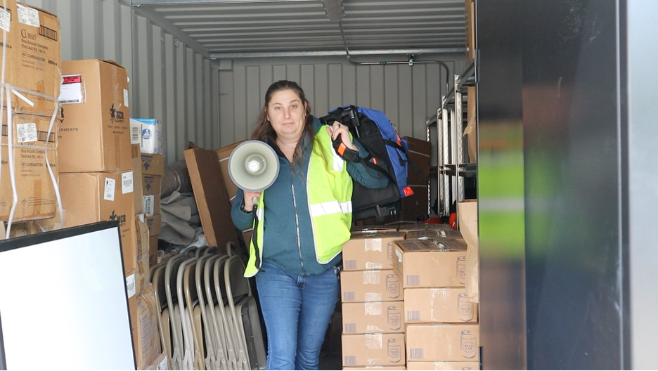 Woman stands holding a backpack and a megaphone.