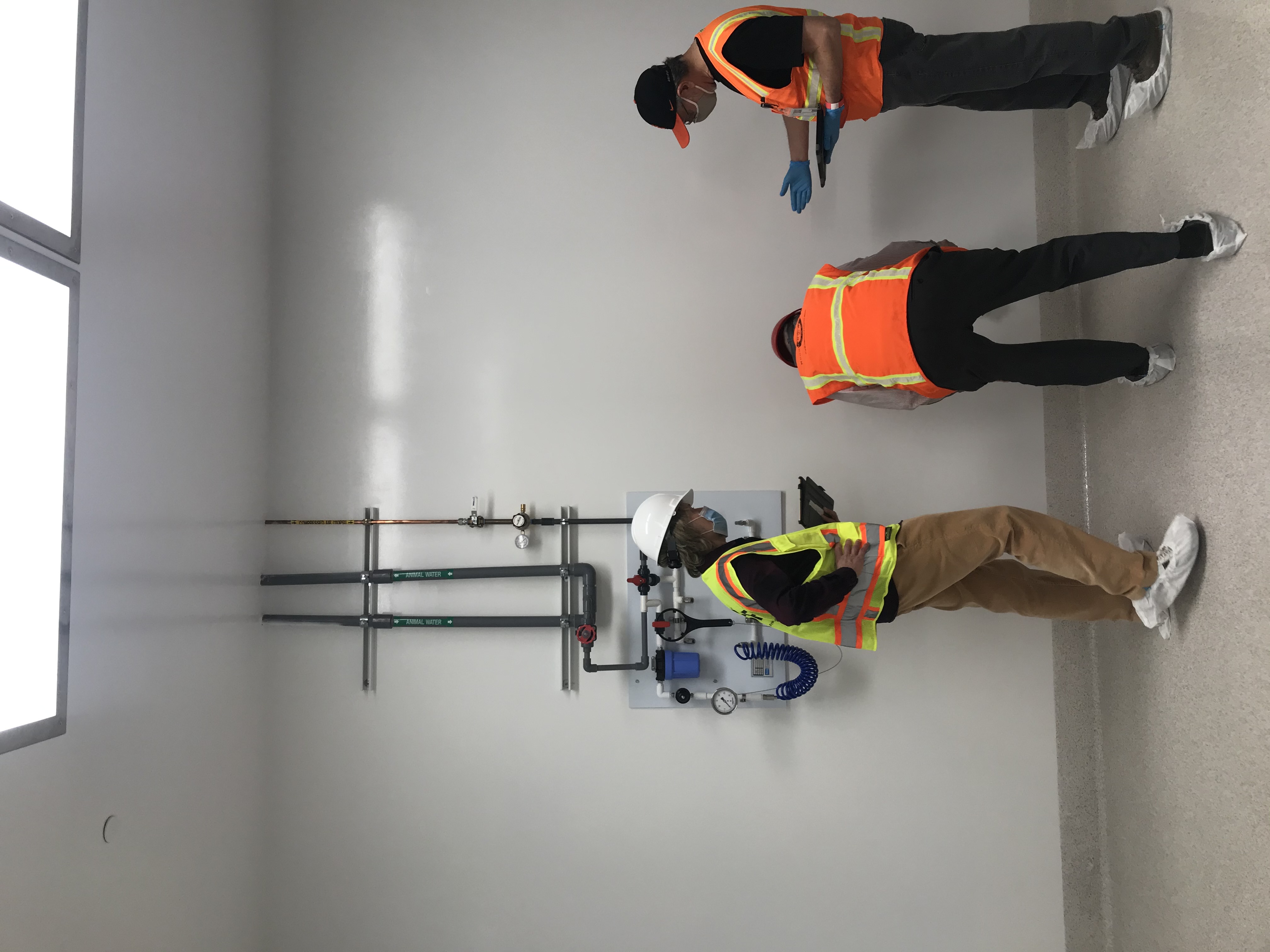 Three people assess machinery while holding clip boards