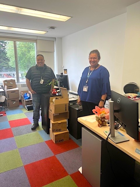 Two employees stand next to boxes
