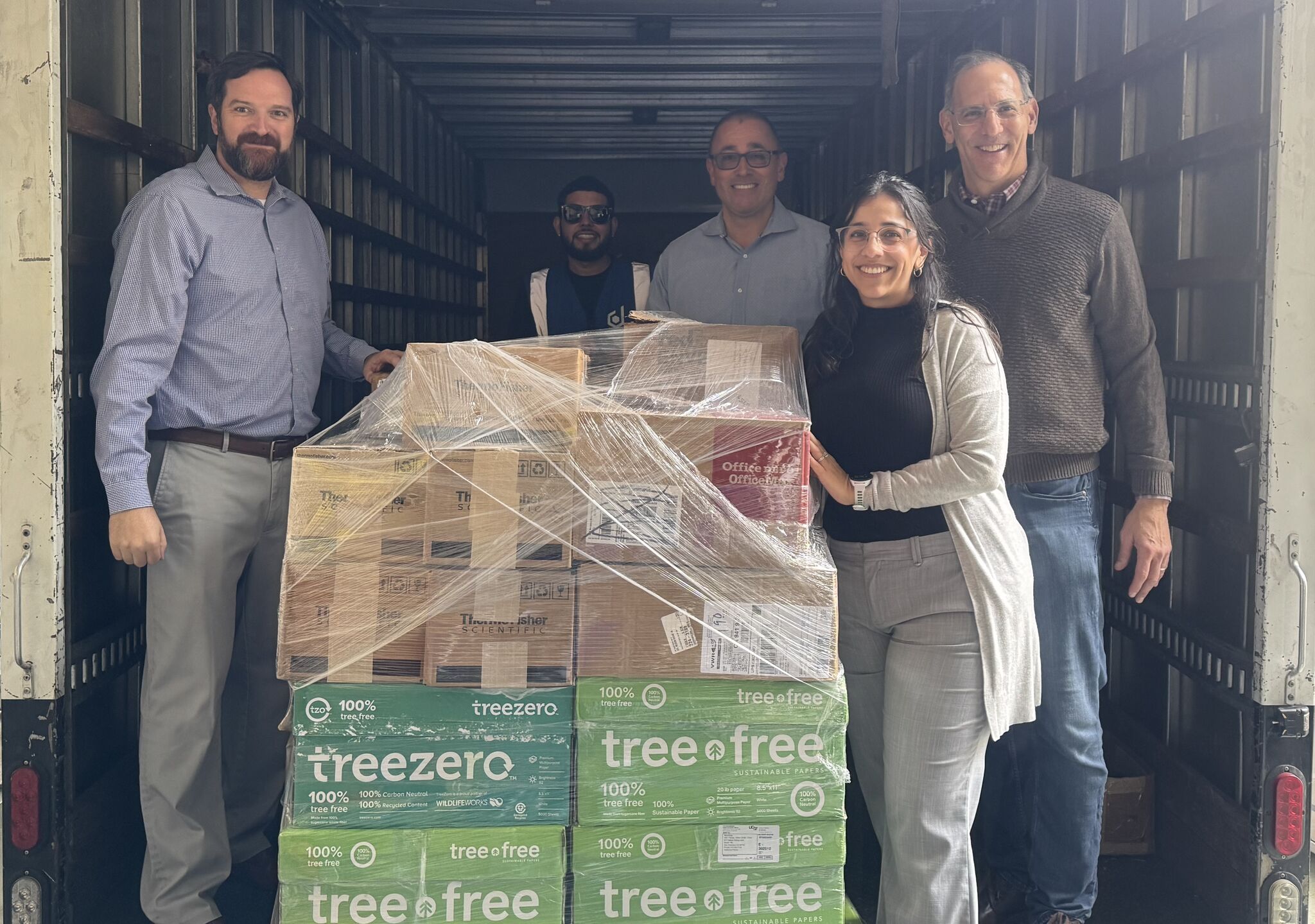 Group stands inside a truck with a stack of wrapped boxes