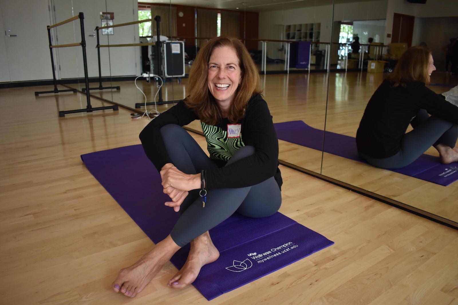 A woman sits cross legged on a yoga mat and smiles