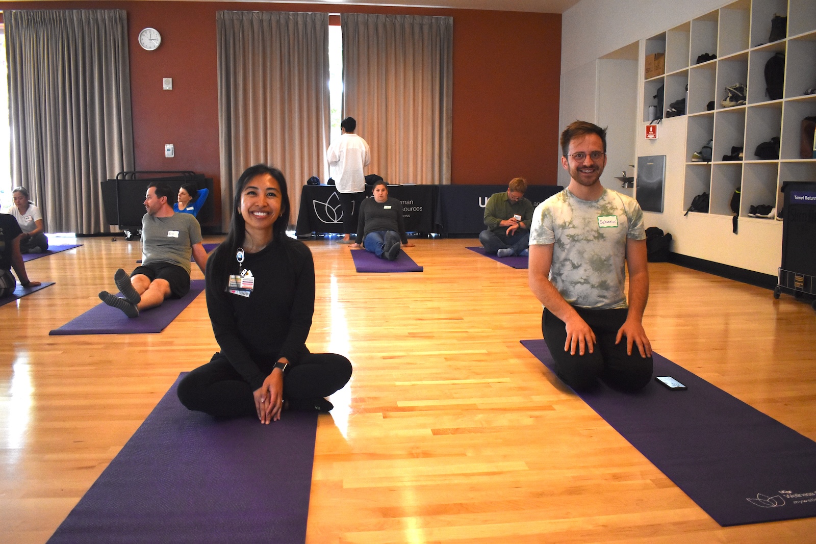 Two people sit on a mat and smile